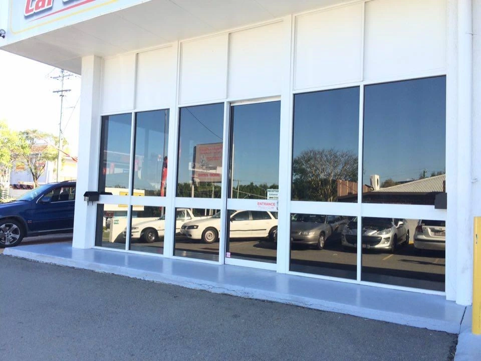 Glass frontage of car service centre reflecting parked vehicles and buildings