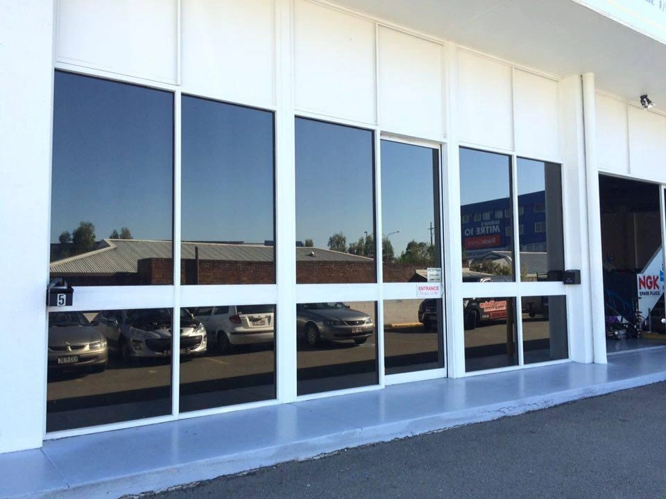 Glass frontage of car service centre reflecting parked vehicles and buildings