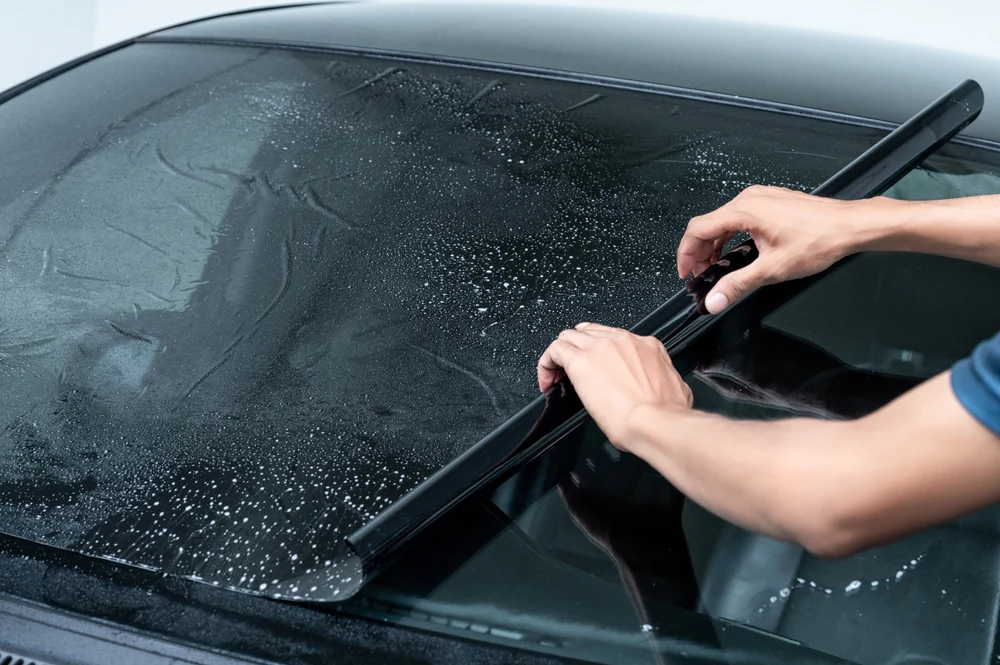 Close-up of hands applying window tint film to a wet car windshield