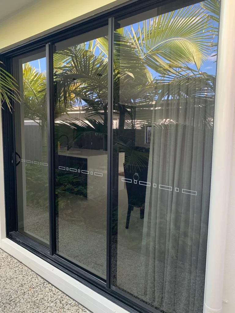 Tinted glass sliding door with palm tree reflections and privacy decals
