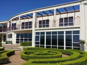 Two-storey home with curved balcony, tall windows, and manicured hedges