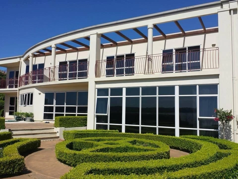 Two-storey home with curved balcony, tall windows, and manicured hedges