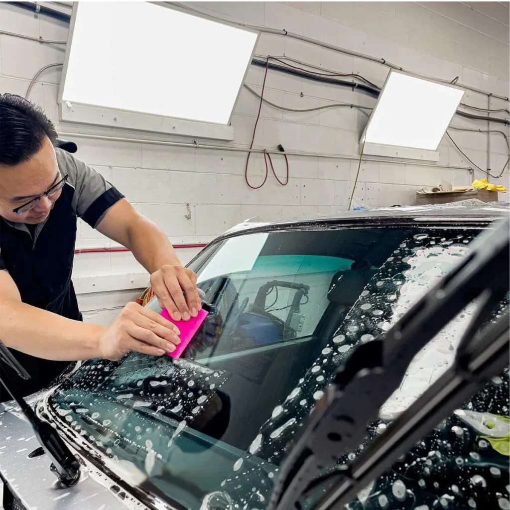 Technician using pink squeegee to clean soapy windscreen before tinting