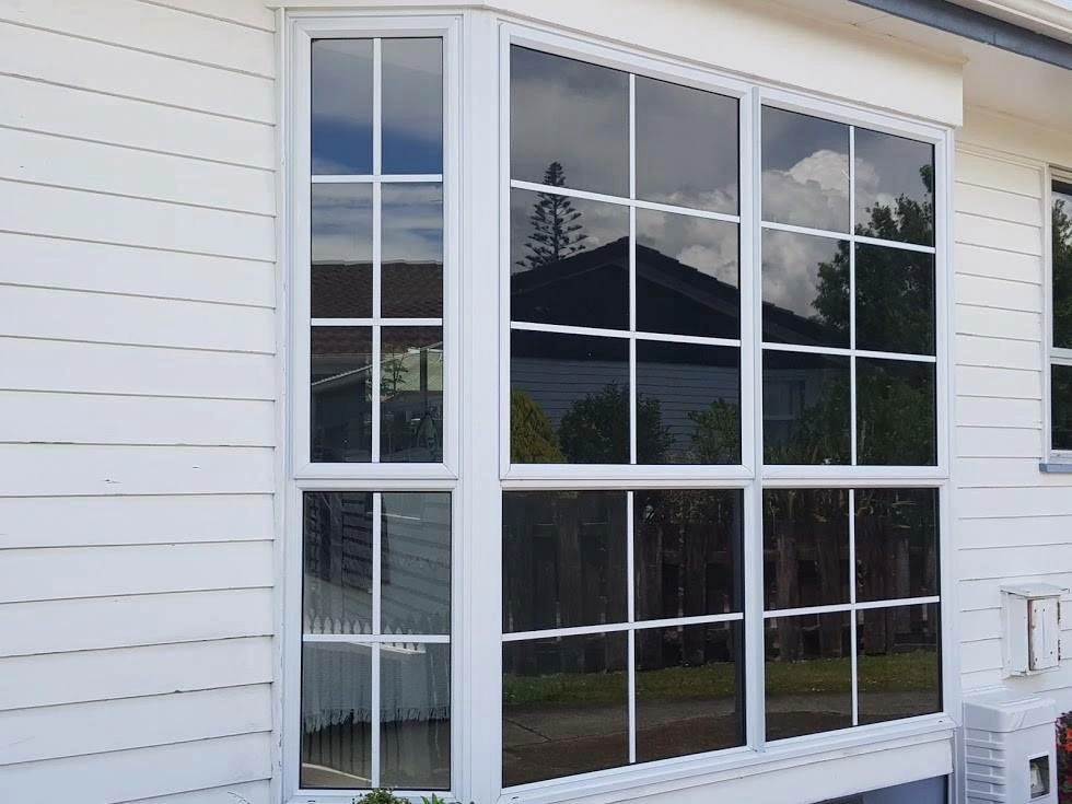 White grid-style window reflecting trees, sky, and neighbouring house