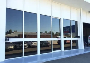Glass frontage of car service centre reflecting parked vehicles and buildings