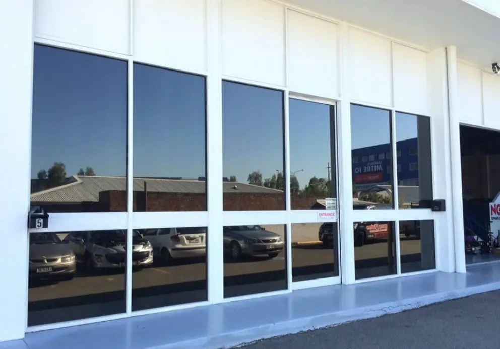 Glass frontage of car service centre reflecting parked vehicles and buildings